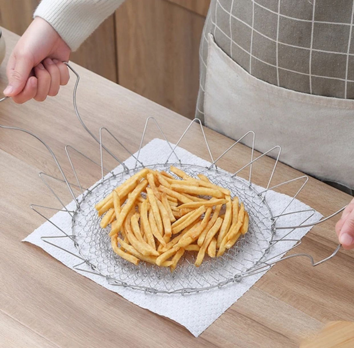 Collapsible stainless steel magic fry basket hanging on a white tile wall, kitchen tool from Zoni Stores