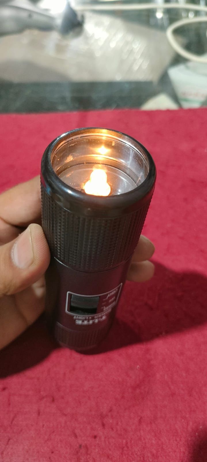Compact LED flashlight held in hand showing the glowing light bulb and switch